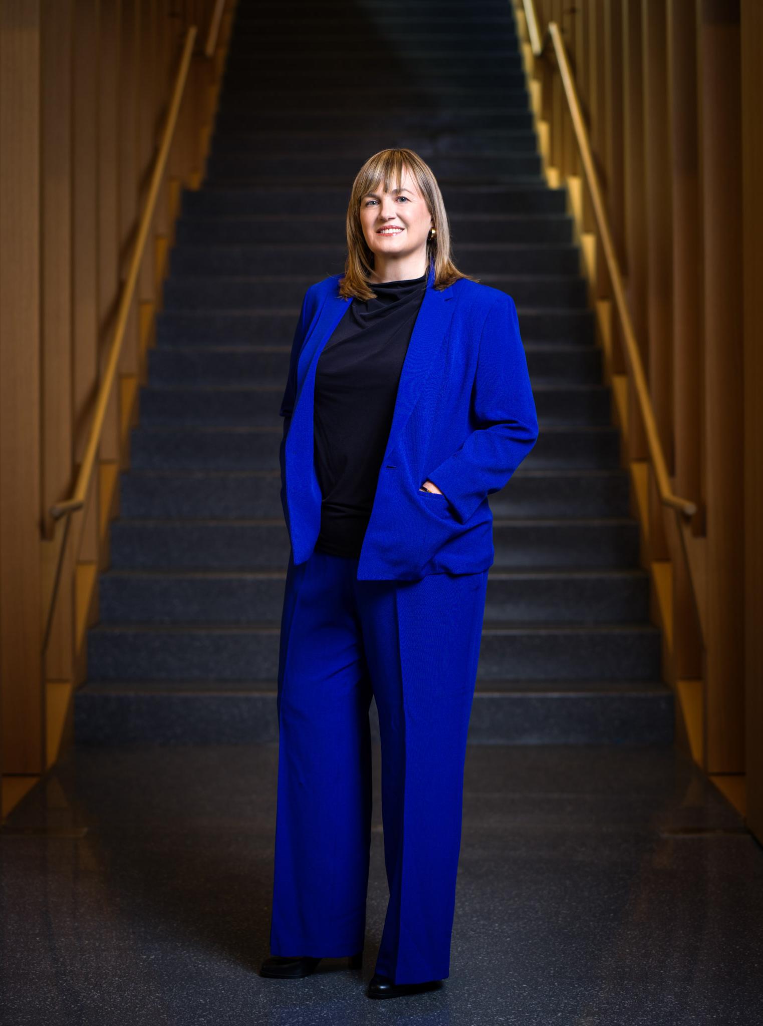President Laura Rosenbury standing in front of the stairs in the Milstein building. She is wearing a blue suit